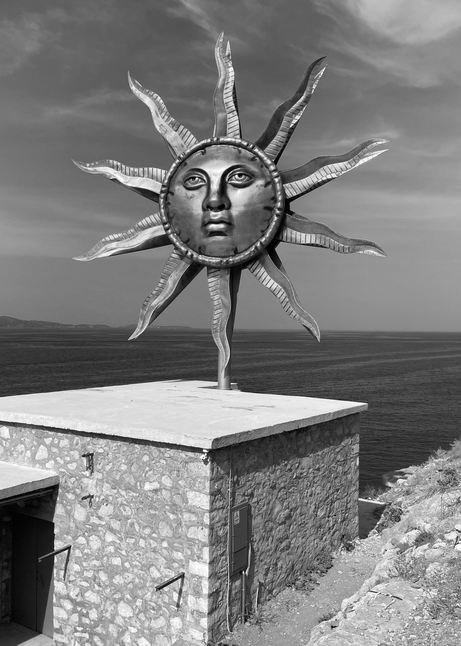Goldene Sonnenskulptur mit Gesicht auf dem Dach eines Steinhauses über dem Meer, Jeff Koons' Apollo Wind Spinner auf Hydra.